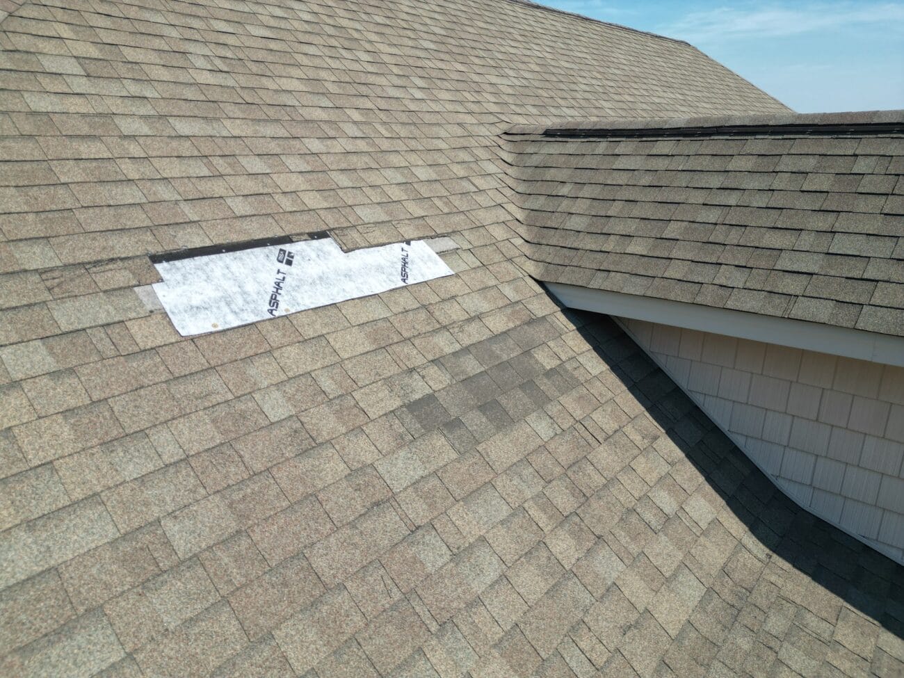 A section of roof shingles is missing, exposing white underlayment, while the rest of the roof appears intact.